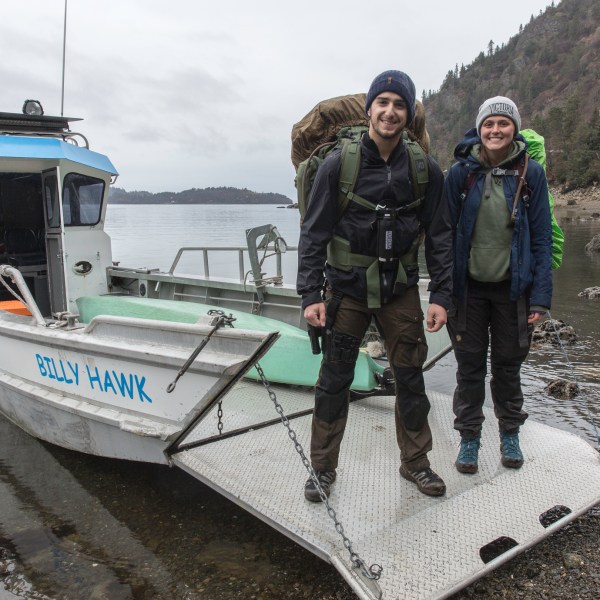 a person standing in front of a boat next to a body of water